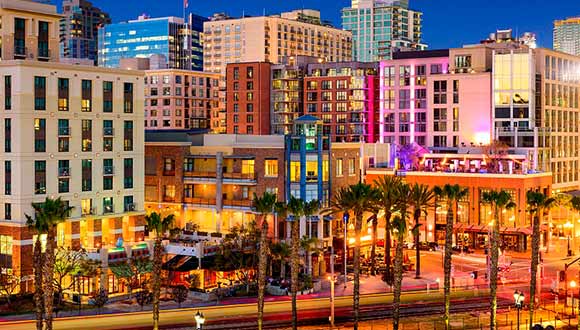 San Diego downtown at dusk, lit up by orange lights, with palm trees in foreground.