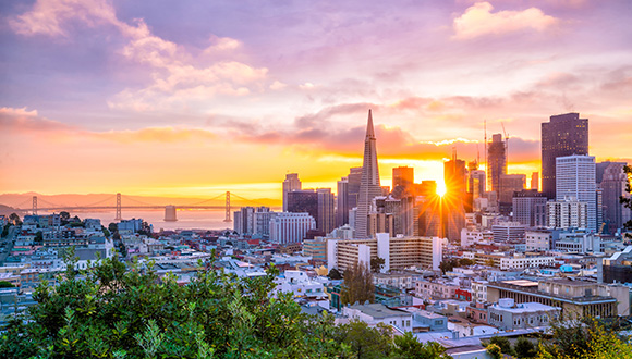 San Francisco skyline at sunset showing skyscrapers, Golden Gate Bridge, and the ocean. 